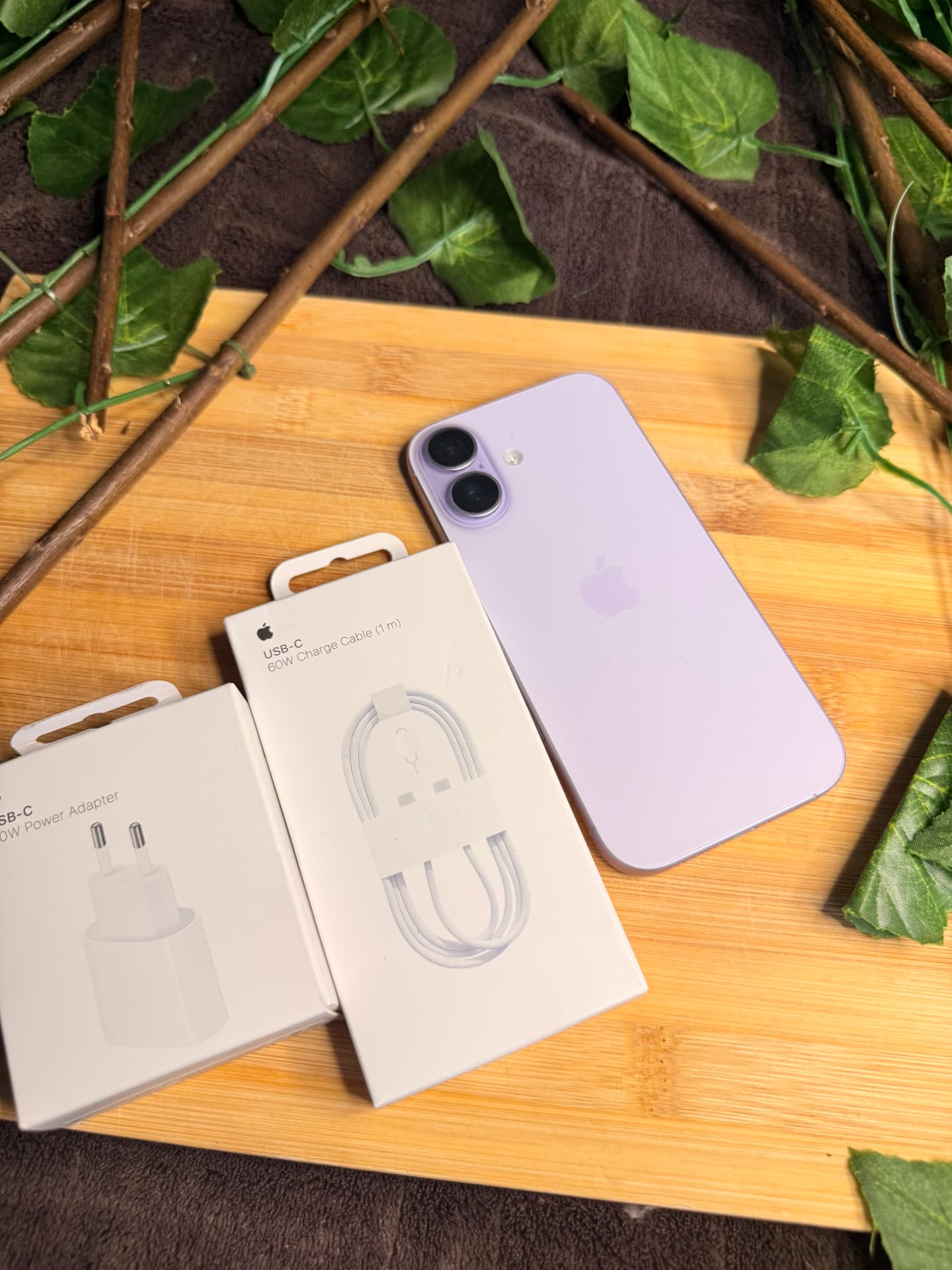 iPhone 16 morado con cargador y cable USB-C sobre tabla de madera